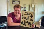 woman leaning on counter holding a sign that reads love what you do