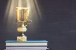 golden trophy on pile of books in front of blackboard