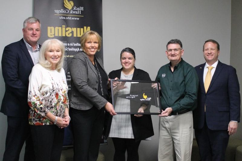 6 people standing in front of nursing banner with framed Black Hawk College pennant