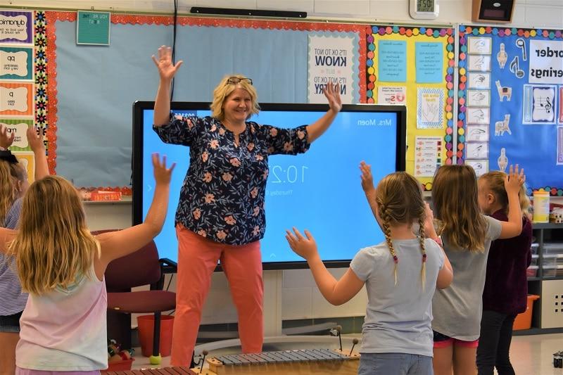 music teacher and students holding their arms up while moving to the beat of a song