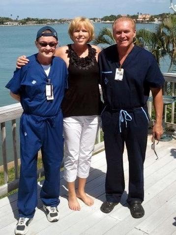 woman with arms around 2 men in scrubs standing on sunny balcony